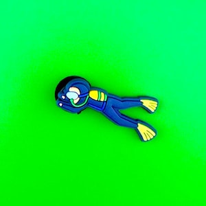 May include: A blue scuba diver pin with yellow flippers, against a green background.