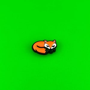 May include: Orange and black cartoon fox charm, curled up sleeping, on a green background.
