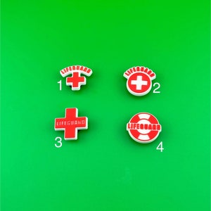 May include: Four white plastic charms with red accents. The charms feature the words "Lifeguard" and a red cross or a red life preserver. The charms are numbered 1 through 4.
