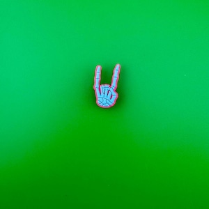 May include: A skeleton hand making the rock and roll hand gesture. The hand is pink and white and is on a green background.