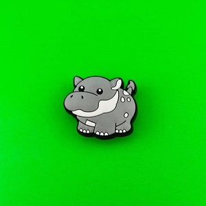 May include: A gray cartoon hippopotamus with white spots and a white mouth. The hippo is standing on a green background.