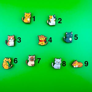 May include: Nine colorful cat charms with different poses and expressions. The charms are numbered 1 through 9.