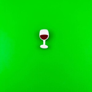 May include: A white wine glass with red wine inside, on a green background.