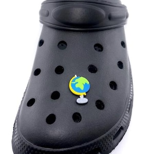 May include: Black clog shoe with a globe charm. The shoe is black with multiple round holes and a textured sole. The globe charm features blue and green continents with a yellow outline.