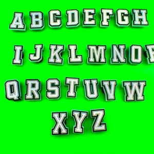 May include: White letters of the alphabet, A through Z, with black outlines, on a green background.