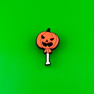 May include: Orange pumpkin shaped Halloween charm with a black jack-o'-lantern face on a white stick.