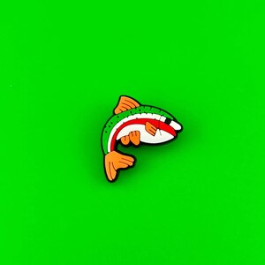 May include: A green, red, and orange fish-shaped charm with a white belly. The charm is made of rubber and has a glossy finish.