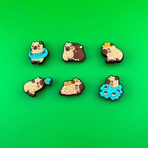 May include: Six colorful cartoon pug dog charms with different poses, including swimming, hugging, and wearing a hat. The charms are made of a soft, rubbery material and are perfect for adding a touch of personality to your belongings.