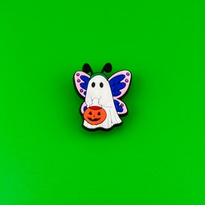 May include: A white ghost with blue and pink butterfly wings holding a small orange pumpkin. The ghost is wearing a green hat.