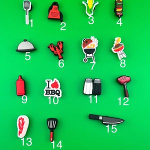 May include: A set of 15 colorful, plastic charms with a barbecue theme. The charms feature images of grilling tools, food, and other barbecue-related items.  The charms are numbered 1 through 15.