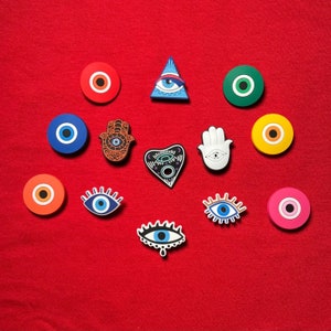 May include: Assortment of colorful eye-shaped charms with various designs, including a hand, a heart, and a triangle. The charms are made of plastic and have a glossy finish.