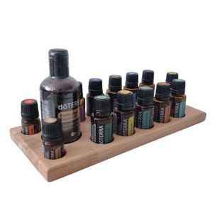 Könnte beinhalten: Ein Holz-Essenzölregal mit 12 Fächern, das 11 bernsteinfarbene Glasflaschen mit Etiketten und eine größere Flasche dōTERRA Fractionated Coconut Oil enthält. Die Flaschen sind in einer Reihe angeordnet, wobei die größere Flasche in der Mitte steht.
