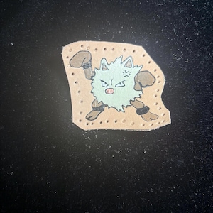 May include: Hand-painted leather patch featuring a cartoon character with a light blue body, brown boxing gloves, and black wristbands. The character has an angry expression. The patch is on a tan background with evenly spaced holes.