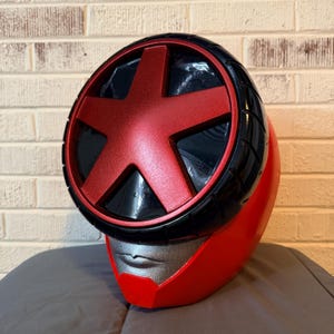 May include: A red helmet with a black and red starburst design on the top. The helmet has a silver faceplate and a red body. The top of the helmet has a black tire-like design.
