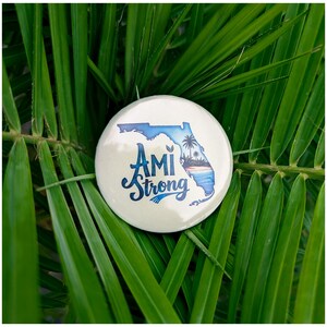 May include: A white button with a blue outline of the state of Florida and the text "AMI Strong" in blue cursive lettering.