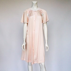 May include: A pale pink, knee-length robe with a button-up front and short sleeves. The robe has white lace trim around the neckline and sleeves.