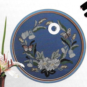 May include: A counted cross stitch pattern for a wreath with blue, white, and green flowers and butterflies. The pattern is titled "Danish Wreaths" and is from "Yours Truly Counted Cross Stitch".