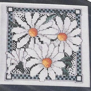 May include: Cross-stitch design featuring four white daisies with orange centers. The flowers are set against a green and black background, framed by a decorative border. The needlework is detailed and the overall effect is a floral theme.