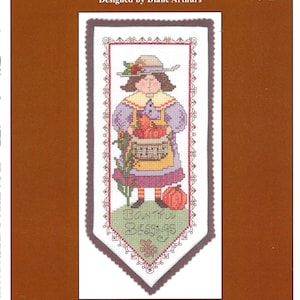 May include: A cross-stitch design titled "Blessings Hang-Up" by Diane Arthurs. The design features a figure holding a basket of pumpkins and the words "Bountiful Blessings". The color palette includes shades of purple, orange, and green.