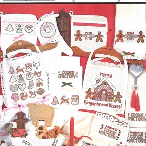 May include: A collection of cross-stitch patterns for kitchen towels and pot holders featuring Christmas and gingerbread themes. The patterns include images of gingerbread houses, reindeer, Santa Claus, and a cookie factory. The text "Merry Gingerbread Kisses!" and "Cookie Factory" are included in the patterns.