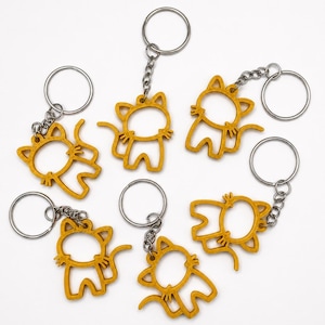 May include: A collection of yellow cat-shaped keychains. Each keychain features a cutout design of a cat with a tail and attached to a silver keyring. The keychains are arranged on a white surface.