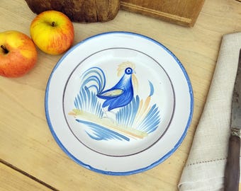 May include: A white ceramic plate with a blue and yellow rooster design. The plate has a blue rim and a white background.