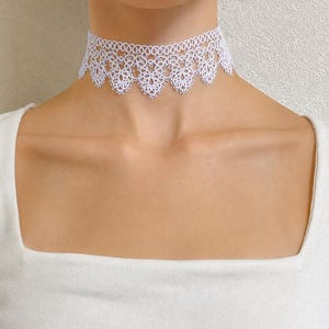May include: A white lace choker necklace featuring an intricate, repeating floral pattern with a scalloped bottom edge. The delicate fabric band sits snugly around the neck, showcasing a detailed needlework design with small, circular openwork loops.
