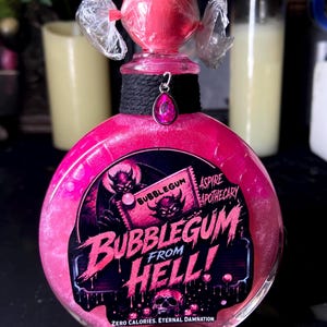 May include: A round glass bottle filled with shimmering pink liquid, topped with a pink candy-like sphere wrapped in clear plastic. A black fabric collar features a pink teardrop charm. The label reads BUBBLEGUM FROM HELL! ASPIRE APOTHECARY.
