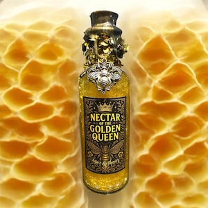 May include: A decorative glass bottle filled with shimmering gold liquid, featuring a detailed label that reads "Nectar of the Golden Queen." The bottle is adorned with a metallic bee emblem and a decorative cap. The background has a honeycomb pattern.