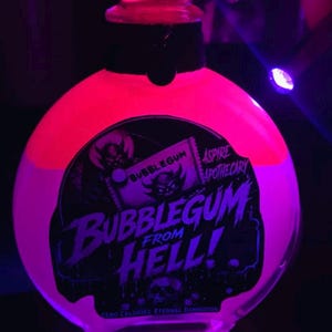 May include: A round glass bottle filled with a glowing neon pink liquid under ultraviolet light. The label features a black graphic with a devil illustration and the text BUBBLEGUM FROM HELL, ASPIRE APOTHECARY, and ZERO CALORIES ETERNAL DAMNATION.