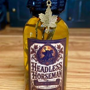 Pode incluir: Uma garrafa de vidro transparente com l&iacute;quido amarelo, selada com cera preta e um pingente de folha de bordo dourada. O r&oacute;tulo apresenta um gr&aacute;fico do Cavaleiro sem cabe&ccedil;a e o texto Headless Horseman, Aspire Apothecary, Pocket Potion Series, Pursuit Risk, High.