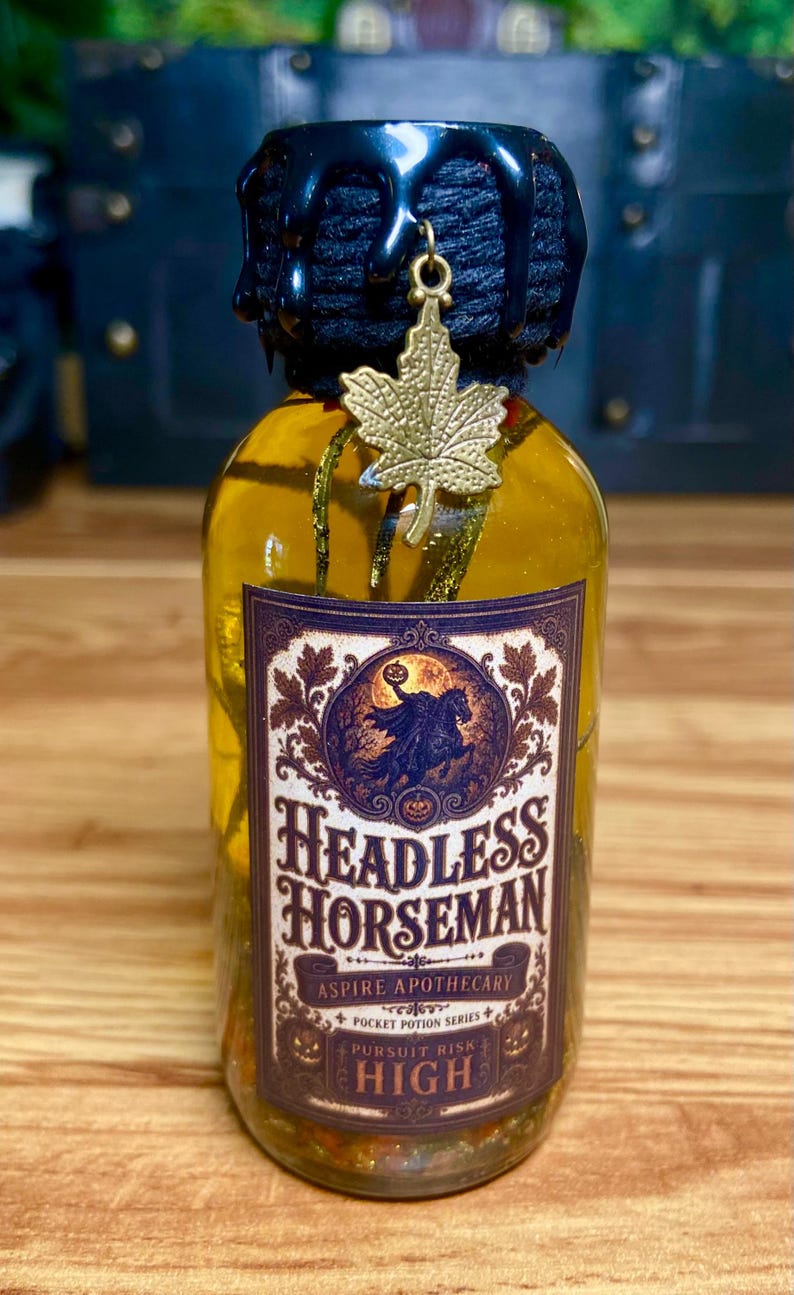 Pode incluir: Uma garrafa de vidro transparente com l&iacute;quido amarelo, selada com cera preta e um pingente de folha de bordo dourada. O r&oacute;tulo apresenta um gr&aacute;fico do Cavaleiro sem cabe&ccedil;a e o texto Headless Horseman, Aspire Apothecary, Pocket Potion Series, Pursuit Risk, High.