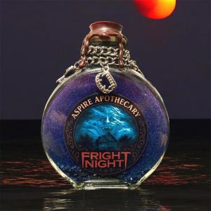 May include: A round glass bottle with a dark purple and blue glitter interior. The bottle has a brown wax seal, a silver chain, and a charm. The label reads "Aspire Apothecary" and "Fright Night" with a spooky illustration.