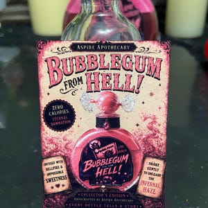May include: A clear glass bottle with a black cap featuring a rectangular label titled BUBBLEGUM FROM HELL! The label displays a pink liquid-filled bottle illustration, text reading ZERO CALORIES ETERNAL DAMNATION, and INFUSED WITH HELLFIRE & IMPOSSIBLE SWEETNESS.