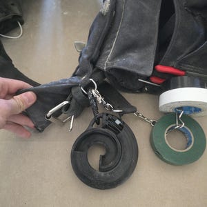 Puede incluir: Un cinturón de trabajo negro con múltiples bolsillos y herramientas adjuntas. El cinturón tiene una hebilla plateada y una variedad de herramientas colgando de él, incluyendo una herramienta en espiral negra, rollos de cinta y una herramienta con mango rojo.