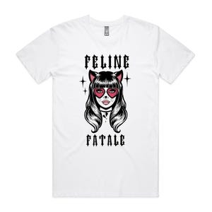 May include: White t-shirt featuring a graphic of a woman with cat ears and heart-shaped sunglasses. The text "FELINE FATALE" is printed above and below the illustration in a gothic font. The shirt is a classic crew neck.