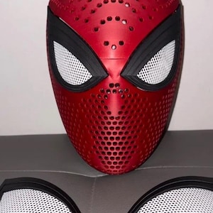 May include: A red full-face mask featuring a perforated texture across the surface, black eye frames, and white mesh lenses. Two additional detachable white mesh lenses with black frames are positioned in front of the mask.