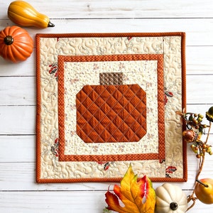 May include: A quilted pumpkin-shaped wall hanging with a brown, orange, and cream colour scheme. The hanging is framed with a decorative border and features a quilted pumpkin design in the centre.