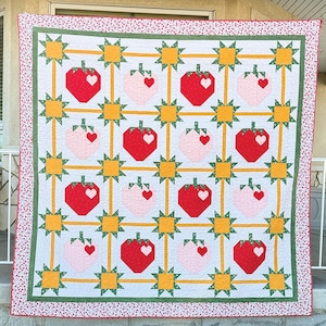 May include: A handmade quilt featuring a repeating pattern of red and pink strawberries with heart-shaped seeds on a white background. The strawberries are connected by yellow lines and surrounded by starbursts. The quilt has a green border and a red and white dotted edge.