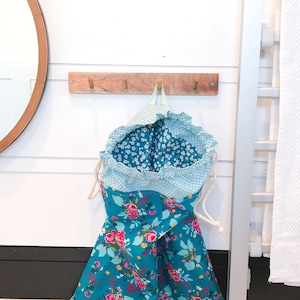 May include: A teal blue laundry bag with a floral print and a white drawstring. The bag is hanging on a wooden hook.