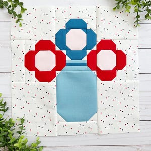 Może przedstawiać: Blok patchwork z niebieskim ważonem i dwoma czerwonymi kwiatami. Kwiaty mają białe środki, a ważon ma biały pasek. Tło jest białe z czerwonymi i niebieskimi kropkami.