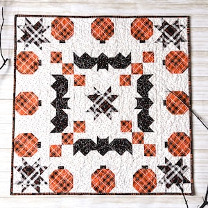 Peut inclure: Une courtepointe blanche avec un motif de patchwork noir et orange. La courtepointe présente des chauves-souris, des étoiles et des citrouilles.