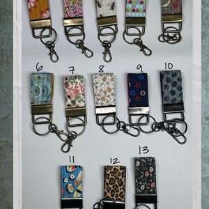 May include: Thirteen fabric key fobs with diverse patterns, including floral, polka dots, and animal prints. Each fob has a metal clasp and key ring. The key fobs are in a variety of colours, such as yellow, pink, blue, and brown.