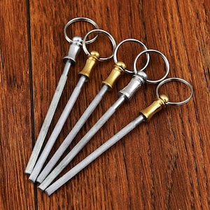 May include: Five silver and gold keychains with a small, thin, metal rod attached to a ring. The rods are sharpened at one end.