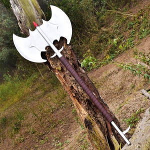May include: A silver axe with a bat-shaped blade and a brown leather wrapped handle. The axe is leaning against a tree trunk.