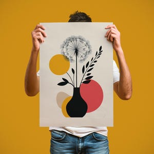 Könnte beinhalten: Ein beigefarbenes Poster mit einer schwarzen Vase mit einem Löwenzahn und Zweigen. Das Design umfasst gelbe, rote und beige geometrische Formen. Das Poster wird von einer Person gehalten, die ein weißes T-Shirt und eine blaue Jeans trägt.