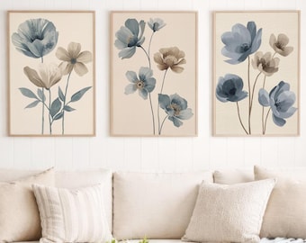 May include: A set of three framed wall art prints featuring watercolour-style blue and beige flowers on a light background, displayed above a beige sofa with a light blue throw blanket and a wooden coffee table with a woven tray and basket.