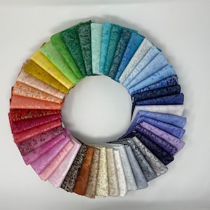 May include: A circular arrangement of fabric squares in a rainbow of colors. The fabrics are folded and fanned out, showcasing a spectrum from yellow to purple, with shades of green, blue, and red. The fabrics have a subtle, textured pattern.