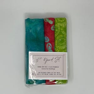 May include: A fabric set with three rolled pieces of fabric in a clear plastic package. The fabrics are teal, red with flip-flop patterns, and green with a floral design. The label reads "3 1/2 Yard Set" and "ONE OF US - 1 1/2 YARDS (extra for binding)".