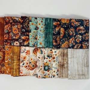 May include: A collection of twenty folded fabric squares featuring various autumn-themed patterns. Designs include orange pumpkins, colorful fall leaves, butterflies, and floral motifs in shades of teal, brown, cream, and gold, alongside textured wood grain prints.